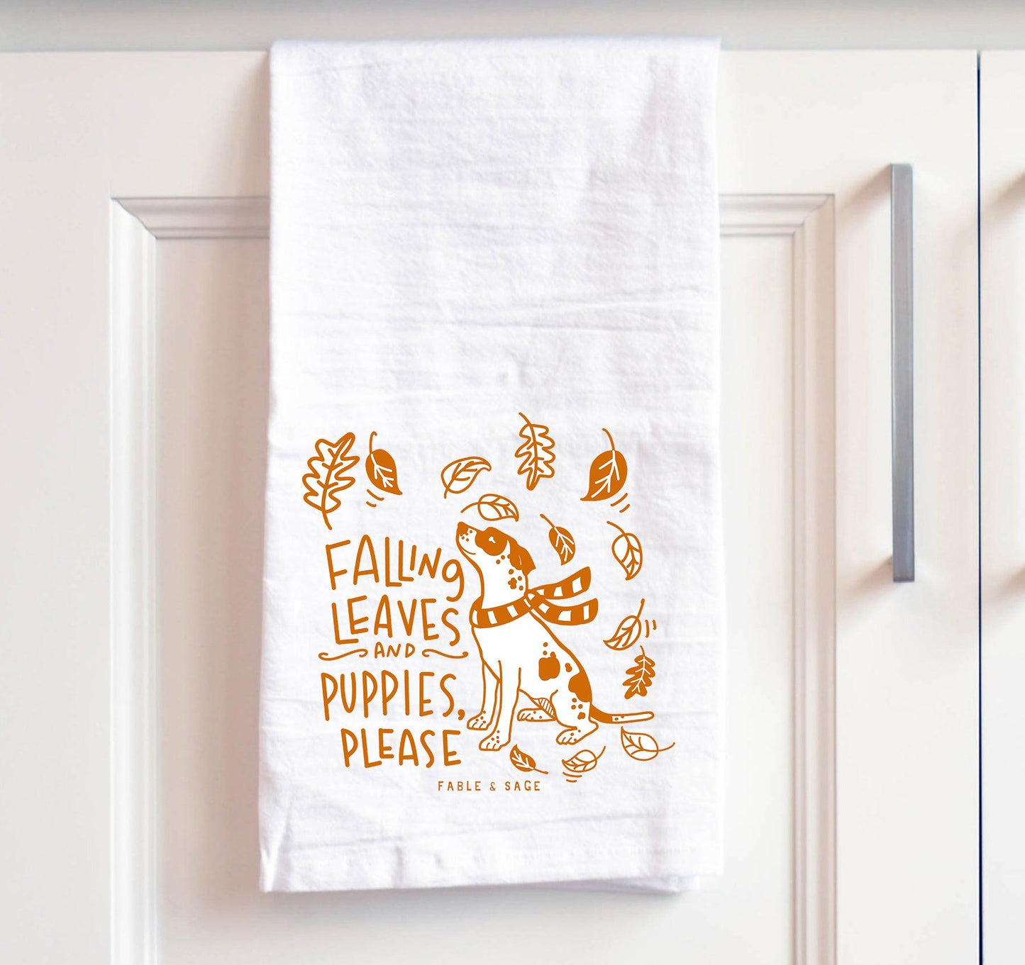 Hand printed kitchen towel of dog and falling leaves displayed on a kitchen cabinet door